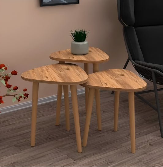 Set of three wooden side tables with a plant on top in a room setting.