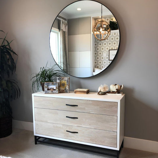 Round mirror above a dresser with decorative items in a room setting.